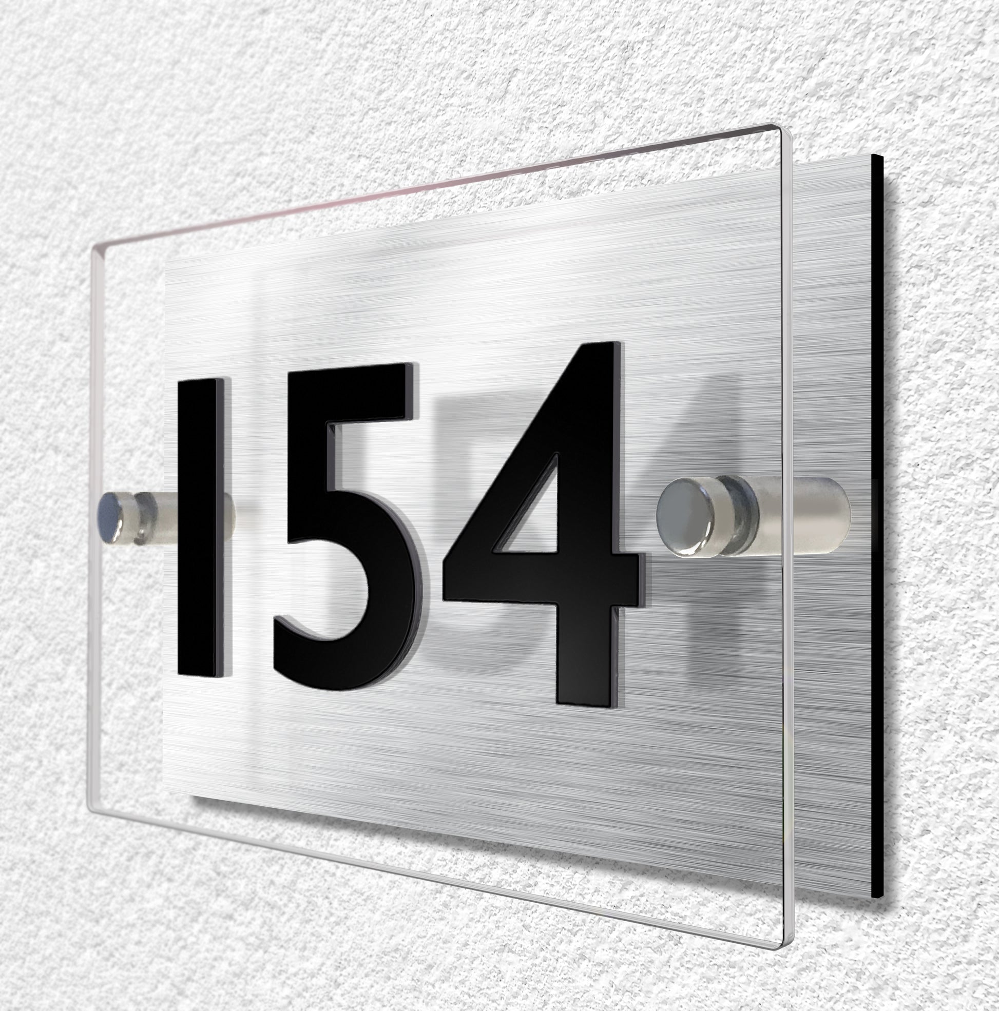 House sign constructed of two layers of material. Brushed aluminium and clear acrylic materials are held separate by stainless steel stand-ff fixings. House number is made from 3mm thick black acrylic and bonded to the clear acrylic for a raised lettering effect.