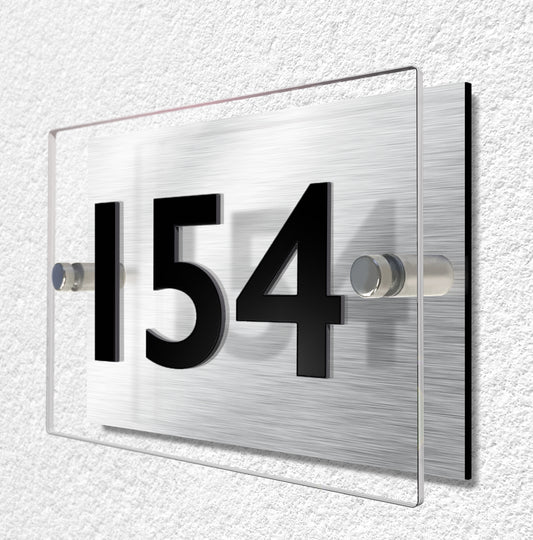 House sign constructed of two layers of material. Brushed aluminium and clear acrylic materials are held separate by stainless steel stand-ff fixings. House number is made from 3mm thick black acrylic and bonded to the clear acrylic for a raised lettering effect.