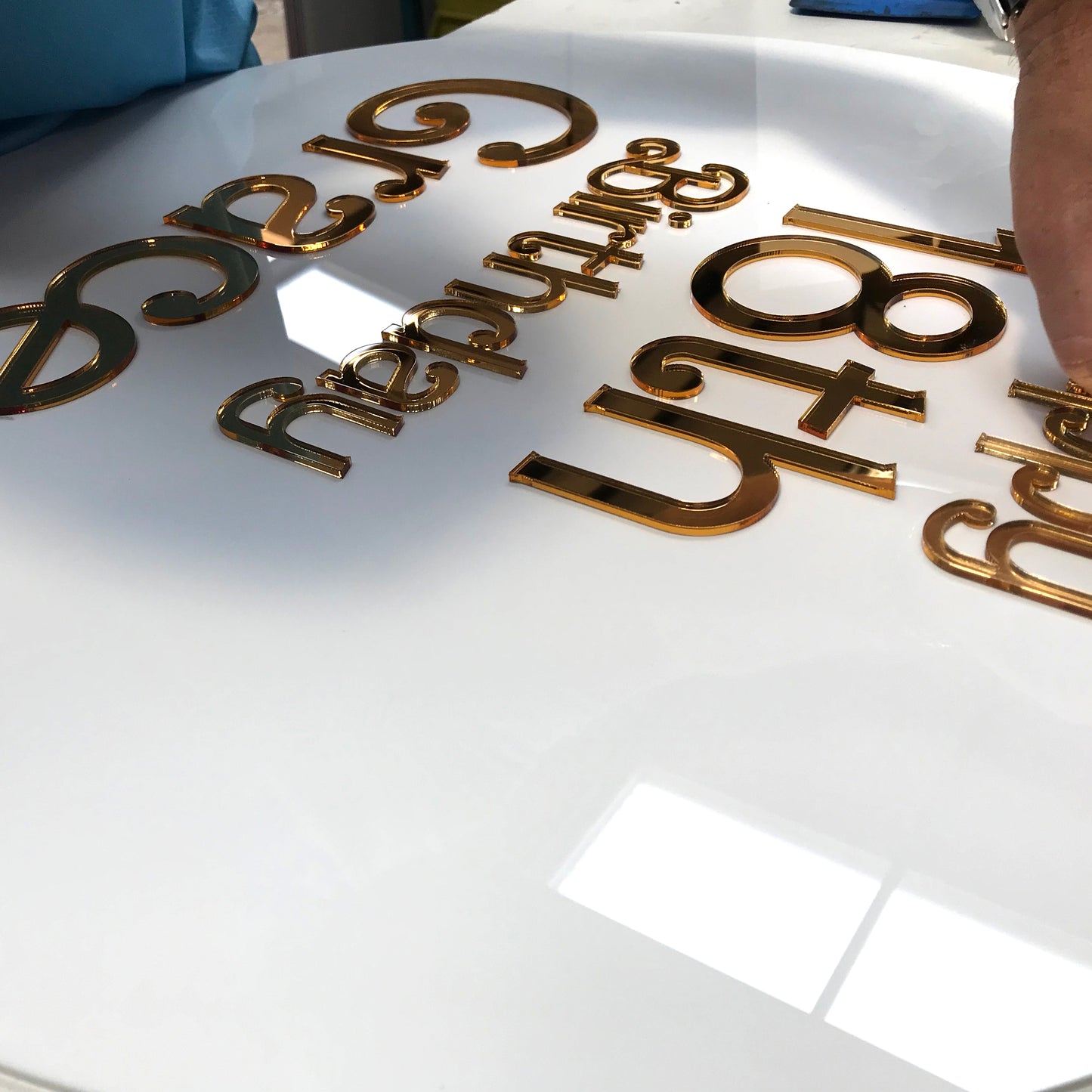 A sign being assembled with laser cut gold acrylic lettering on a round sign panel