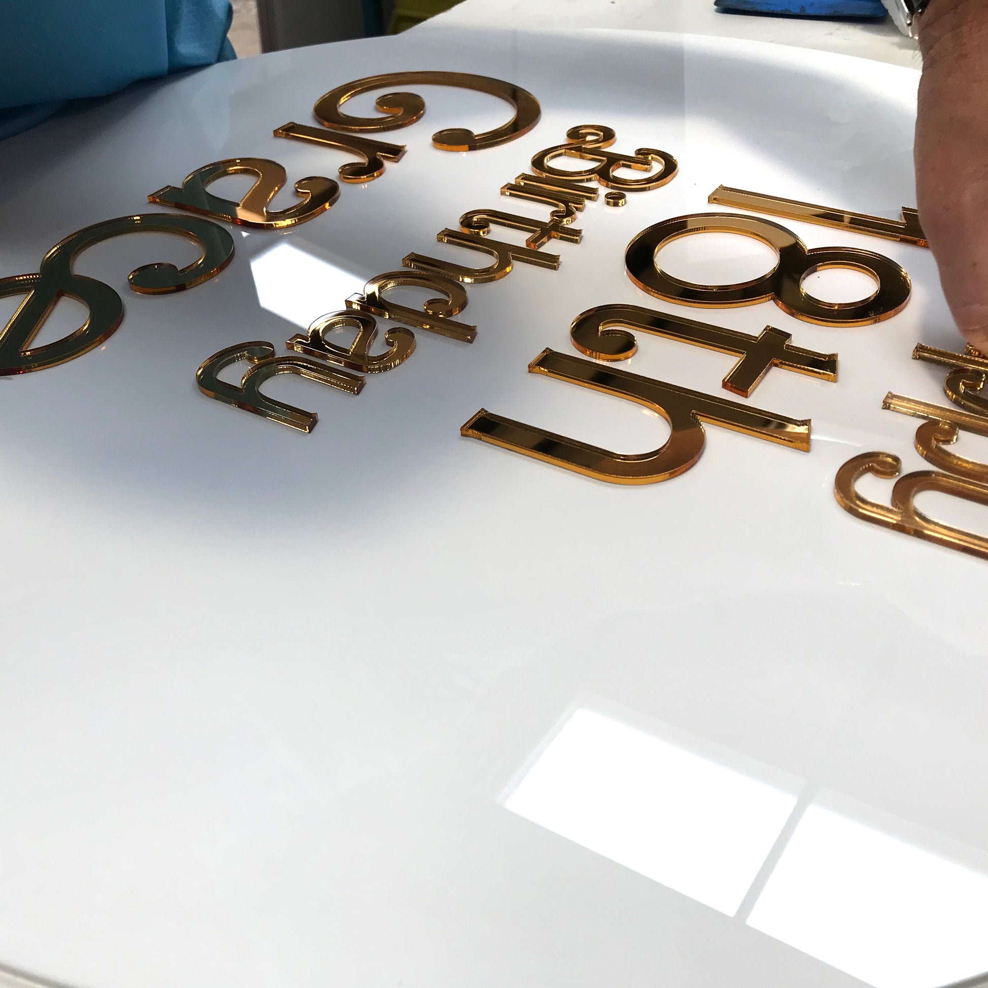 A sign being assembled with laser cut gold acrylic lettering on a round sign panel